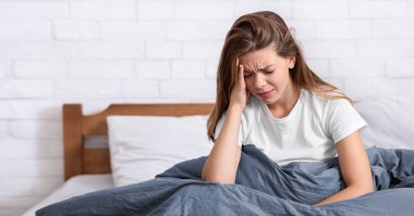 Akıl sağlığı sorunları konsepti. Mutsuz genç bir kadın yatağında oturmuş depresyon ya da uykusuzluk çekiyor, korkunç bir baş ağrısı çekiyor, olumsuz düşüncelerle boğuşuyor.