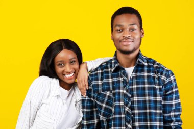 Öğrencilerin mutlu bir ilişkisi ve kovid 19 tecridi sırasında birlikte eğlenmeleri. Gülümseyen Afrikalı genç bir Amerikalı kadın ve erkek kameraya bakar, kadın elini erkeğin omzuna koyar, sarı arka planda izole olur.