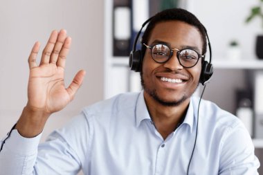 Ofis çalışanı konsepti. Kameraya, ofis içine ve boş alana el sallayan mutlu Afrikalı Amerikalı adam danışmanı. Çevrimiçi çalışan, gözlük takan neşeli siyahi işveren.