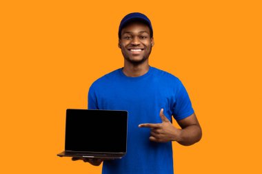 Teslimat Servisimizi Seç. Afro-Amerikan kurye elinde dizüstü bilgisayarı olan, mavi şapkalı ve üniformalı, turuncu arka planda izole edilmiş siyah boş ekrana bakan bir adam.