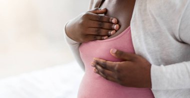 Hamilelik rahatsızlığı. Siyahi hamile kadın göğüs ağrısı çekiyor, Afrikalı hamile kadın evde otururken kendine masaj yapıyor, seçici bir odak ile kırpılmış görüntü, yakın çekim.