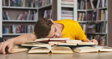 Kütüphanede uyuyor. Yorgun beyaz adam kitap yığınında şekerleme yapıyor, sınavlara hazırlanırken yoruluyor