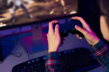 Bir insan elleri, parmakları tuşların üzerinde dinlenen, renkli bir ekranla aydınlanan bir bilgisayar ekranında oyun oynayan siyah bir video oyunu denetleyicisini tutar..