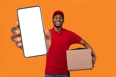 Hızlı Sevkiyat Konsepti. Kırmızı şapkalı ve üniformalı, elinde karton kutu olan ve turuncu stüdyo duvarının üzerinde duran Afro-Amerikan teslimatçı çocuk portresi.