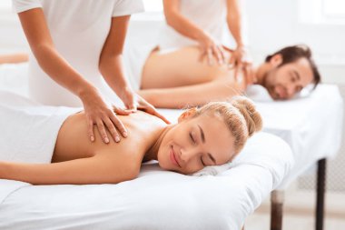 Rahatlamış eşler, kapalı bir kaplıcadaki bir güzellik merkezinde yatağında sırt masajının keyfini çıkarıyorlar. Masörlerin eşlerine masaj yapması. Haftasonu sağIık gevşemesi. Seçici Odaklanma