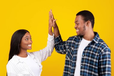 Ortaklık, takım çalışması ve işbirliği. Gülümseyen Afro-Amerikalı erkek ve kadın öğrenciler, sarı arka planda, boş alanda, stüdyo çekimlerinde izole bir şekilde beşlik çakıyor.