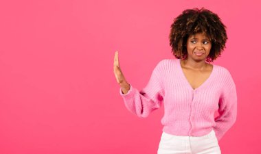 Sad confused millennial african american curly woman in casual show hand stop sign, isolated on pink background, studio, panorama. Emotions, disgust, rejection, fight with harassment, discrimination