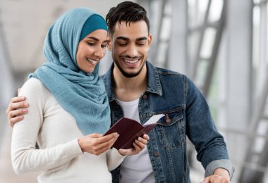 Mutlu İslamcı eşler, havaalanında uçuş beklerken pasaportlarını ve biletlerini kontrol ederken, tesettürden zevk alan genç Arap erkek ve kadın, tatil gezisine hazır, fotokopi alanı ile yakın çekim
