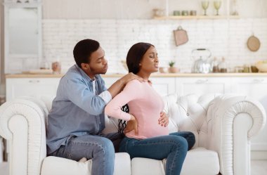 Siyah hamile kadın sırt ağrısı çekiyor, sevgili kocası evde omuzlarına masaj yapıyor. Afrikalı Amerikalıyı önemseyen bir adam hamileliği sırasında gerginliği atmak için karısına masaj yapıyor.