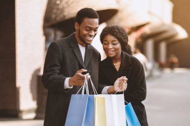 Mutlu binlerce yıllık Afro-Amerikan çifti Kara Cuma ve sezon satışlarından keyif alıyor. Adam renkli paketleri açıyor ve kadın alışverişlerine şehir merkezinin yakınındaki dükkanda yer gösteriyor.