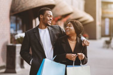 Mevsimsel indirimde ve Kara Cuma 'da birlikte vakit geçiririz. Tatmin olmuş binlerce yıllık Afro-Amerikan erkeği ve renkli çantalı kadın alışveriş merkezinin yakınında gülüp birbirlerine bakıyorlar.