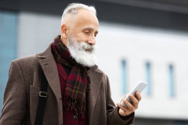 Yakışıklı gri saçlı iş adamı işten eve geliyor, akıllı telefon ekranına bakıyor, e-postaları kontrol ediyor ya da mesajları okuyor, kopyalama alanını kopyalıyor. Varlıklı kıdemli adam caddede cep telefonunu kontrol ediyor.