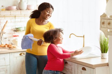 Küçük Yardımcı. Anne ile yemek yedikten sonra bulaşık yıkayan sevimli siyah kreş kızı, sevimli Afro-Amerikan bayan çocuk, evde, boş alanda annesine yardım ediyor.