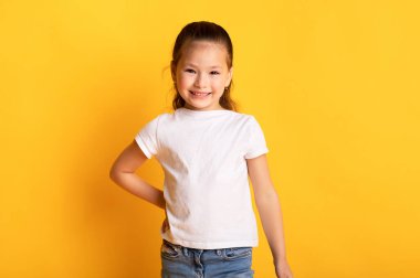 Küçük bayan manken. Kameraya bakıp el ele tutuşan kendine güvenen Asyalı bir çocuk. Kameraya bakan sevimli bir kız, sarı stüdyo arka planında tek başına duruyor, boşluğu kopyalıyor.