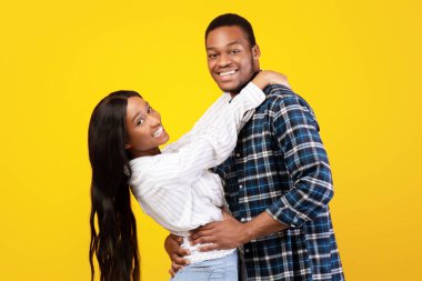 Neşelenin, buluşun, eğlenceli dans edin ve eğlenin. Milenyum mutlu Afrikalı Amerikalı öğrenciler. Karı koca eğleniyor ve sarılıyorlar. Sarı arka planda izole edilmiş, boş alan, stüdyo çekimi.
