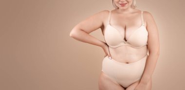 Kendini kabullenme. Stüdyoda bej arka planda güzel kıvrımlı kadın, iç çamaşırlı beden pozu artı beden ölçüsü, doğal güzelliğinin tadını çıkartıyor, fotokopi alanı ile kesilmiş görüntü.