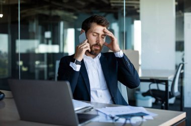 Endişeli erkek girişimci cep telefonuyla konuşuyor ve stresli bir şekilde kafasına dokunuyor, endişeli orta yaşlı işadamı işle ilgili sorunlar yaşıyor, rahatsız edici bir cep telefonu görüşmesi yapıyor.