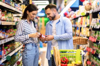 Super Market Konseptindeki Müşteriler. Genç bir çift süpermarkette alışveriş yapıyor sağlıklı ürünler seçiyor markette alışveriş arabasıyla birlikte yürüyor ve birlikte yemek alıyor.