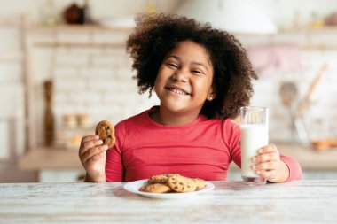 Afro-Amerikan tatlı kız portresi, mutfakta kurabiye ve sütten hoşlanan, evde abur cubur yiyen güzel siyah çocuk, taze bisküvi ve kalsiyum içeceği ile bir ısırık alan anaokulu çocuğu,