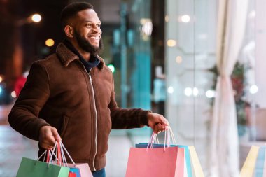 Mutlu Müşteri. Merkezdeki alışveriş merkezinin vitrinine bakan heyecanlı siyahi adam. Alışveriş yaptıktan sonra elinde çantalarla dışarıda duran gülen yakışıklı adam. Mevsimlik Satış, Teklif ve İndirim