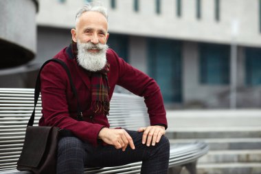 Yakışıklı, şık kıyafetli, şık sakallı adam bankta oturuyor, kameraya gülümsüyor, fotokopi çekiyor. Mutlu yaşlı işadamı boş zamanlarının tadını çıkarıyor, sokakta temiz hava soluyor.