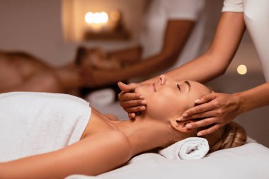 Rahatlatıcı Çiftler Terapisi sırasında kadın yüz masajı alıyor. Kapalı Kaplıcada, yatakta uzanıp tedavinin tadını çıkarıyor. Egzotik Masaj ve Güzellik Ritüeli. Seçici Odaklanma