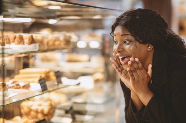 Modern marketlerde tatlı ve kek için düşük fiyatlar. Şaşırtıcı bir şekilde mutlu bin yıllık Afro-Amerikan kadını hamur işleriyle vitrinlere bakıyor ve onları indirimli, kapalı, bedava almak istiyor.