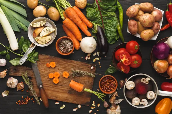 Yemek malzemeleri arka planında. Kesme tahtasında dilimlenmiş havuç ve antika bıçak, sebzeler, şifalı otlar ve mutfak masasında baharatlar. Vejetaryen mutfağı ve yemek hazırlama konsepti.