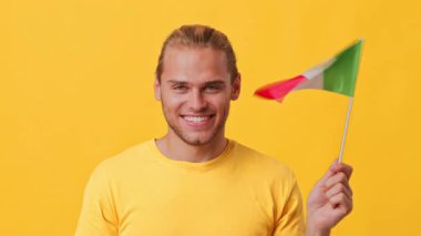 Neşeli genç bir adam parlak sarı bir gömlek giyerken küçük bir İtalyan bayrağı tutuyor. Neşeli ifadesi canlı bir arka planda heyecan yayıyor, kültüre olan hevesini gösteriyor..