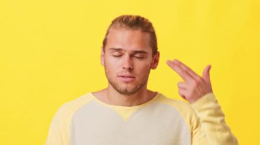 Açık renk saçlı ve günlük kıyafetli genç bir adam parlak sarı bir arka plana karşı duruyor. Yüzü sakin ve cezbedici, sakin ama özenli bir tavır sergiliyor..