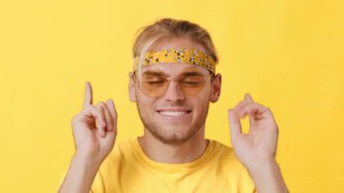 Enerjik bir ortamda, genç bir adam havalı bir güneş gözlüğü ve eğlenceli bir saç bandı takmış, kendine güveni ve gençlik ruhunu canlı sarı bir arka plana karşı geniş bir şekilde gülümsüyor..