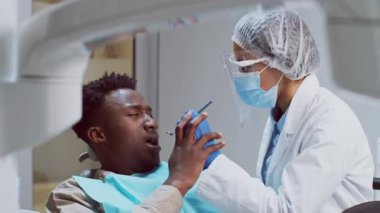 Afrikalı bir Amerikalı dişçi, iyi donanımlı bir diş kliniğinde bir hastayı tedavi etmeye odaklanır. Profesyonel koruyucu giysi giyerken aynı zamanda hasta konforunu sağlıyor..