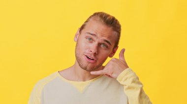 Melez kökenli şık bir genç adam eliyle telefon işareti yapıyor. Parlak sarı bir arkaplanda duruyor, rahatlamış ve dost canlısı bir hava yayıyor..