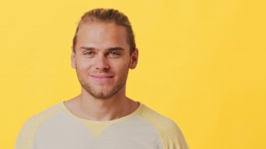 Şık bir saç kesimi olan neşeli bir genç adam iyi bir jest yaparken sıcak bir şekilde gülümser. Parlak sarı bir arka planın önünde duruyor, pozitif enerji ve güven yayıyor..