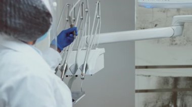 Bir Afrikalı Amerikalı dişçi koruyucu giysiler giyerken diş aletleri düzenliyor. Diş sağlığı kliniğinde, sağlık standartları ve hasta güvenliğini vurgulayan modern ekipmanlar yer alıyor..