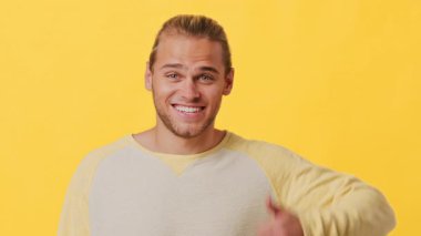 Hevesli bir gülümsemesi ve kendine güvenen bir başparmağı olan genç bir adam, parlak sarı bir arka plana karşıdır. Onun günlük kıyafetleri neşeli atmosferi tamamlıyor, pozitifliği yakalıyor..