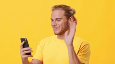 Sıradan saç stili olan neşeli bir adam akıllı telefonunu kontrol ediyor ve bir anlık bağlantının tadını çıkarıyor. Parlak sarı arka plan, genç izleyiciler için mükemmel olan canlı atmosferi arttırır..