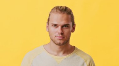 Afrika ve Kafkas mirası karışımına sahip genç bir adam parlak sarı bir arkaplanın önünde güvenle duruyor. Günlük kıyafetleri Z jenerasyonunun tipik bir rahatlama titreşimini yansıtıyor..