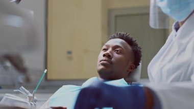 Afrika kökenli Amerikalı bir dişçi, iyi donanımlı bir diş kliniğinde bir hastaya bakım sağlar. Çevre temiz ve düzenli, bu da sağlık hizmetlerinde mükemmelliği yansıtıyor..
