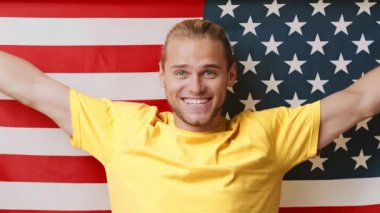 Neşeli bir yüzü olan genç bir adam gururla Amerikan bayrağının önünde duruyor..