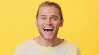 Neşeli bir suratı olan genç bir adam gündelik giyinirken mutluluğunu sergiliyor. Açık kahverengi saçları parlak sarı arkaplanı tamamlıyor ve canlı bir atmosfer yaratıyor..