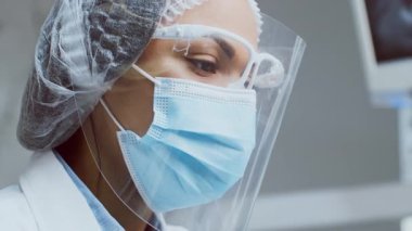 Bir Afrikalı Amerikalı dişçi, temiz ve modern bir klinikte koruyucu giysiler giyerken diş aletleri hazırlar. Konferansta hasta güvenliği ve prosedürler sırasında yüksek kaliteli bakımın sağlanması üzerinde duruluyor.