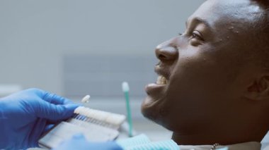 Afro-Amerikalı bir dişçi dişçi, dişçi kliniğinde bir hastaya bakar ve kendisini oral sağlığa adamış profesyonel bir çevreyi gösterir..