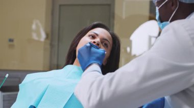 Bir Afrikalı Amerikalı dişçi diş muayenesi sırasında bir hastayla temas kurar. Kurulum, profesyonel bir atmosferi güvence altına alan, sağlık ekipmanlarıyla birlikte modern bir diş sağlığı kliniği..