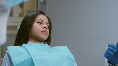 Genç bir kadın, dişçiyle görüşmesini beklerken sakin ama odaklanmış bir şekilde modern bir diş kliniğinde oturuyor. Klinikte çağdaş dekor ve ekipmanlar yer alıyor..