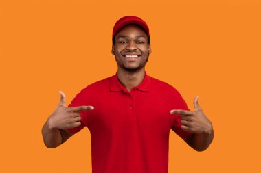 En iyi teslimat işçisi. Neşeli Sakallı Kara Kurye 'nin portresi kendini işaret ediyor, kırmızı tişört giyiyor, iş ilanı veriyor, Orange Stüdyoları' nın arkasında duruyor ve poz veriyor.