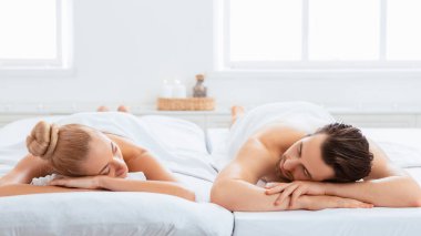 Masaj terapisinden sonra Spa 'da dinlenen rahat bir çift. Beyaz Havlulara Sarılı Eşler Yenilenme Güzelliği Tedavisinden Sonra Dinleniyor. Romantik Rahatlama. Panorama