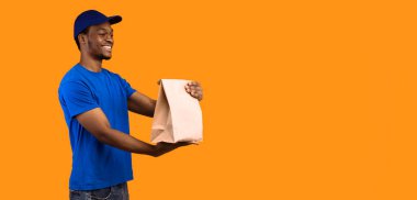 Hızlı Teslimat. Mavi şapkalı, gülümseyen Afro-Amerikan teslimatçı adam. Restorandan el çantasına fotokopi alanı ve turuncu arka planı olan ürünler veriyor.