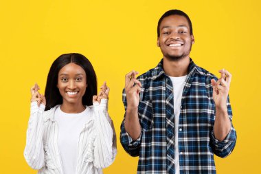 Hayal, büyük arzu ve kazanmak istiyorum. Mutlu, genç, Afro-Amerikan karı ve koca dua eder ve bir dileğin gerçekleşmesi için dua eder, sarı arka planda izole edilmiş, stüdyo çekimi, boş alan.