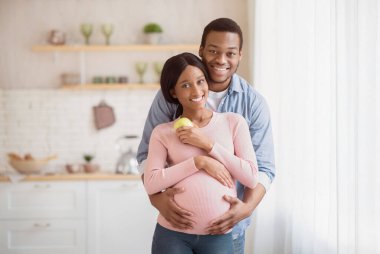 Sevgi dolu siyah koca portresi hamile karısına evde sarılıyor. Elmalı ve kocasıyla kucaklaşan güzel, hamile bir kadın. Afrikalı Amerikalı çift bebek bekliyor.